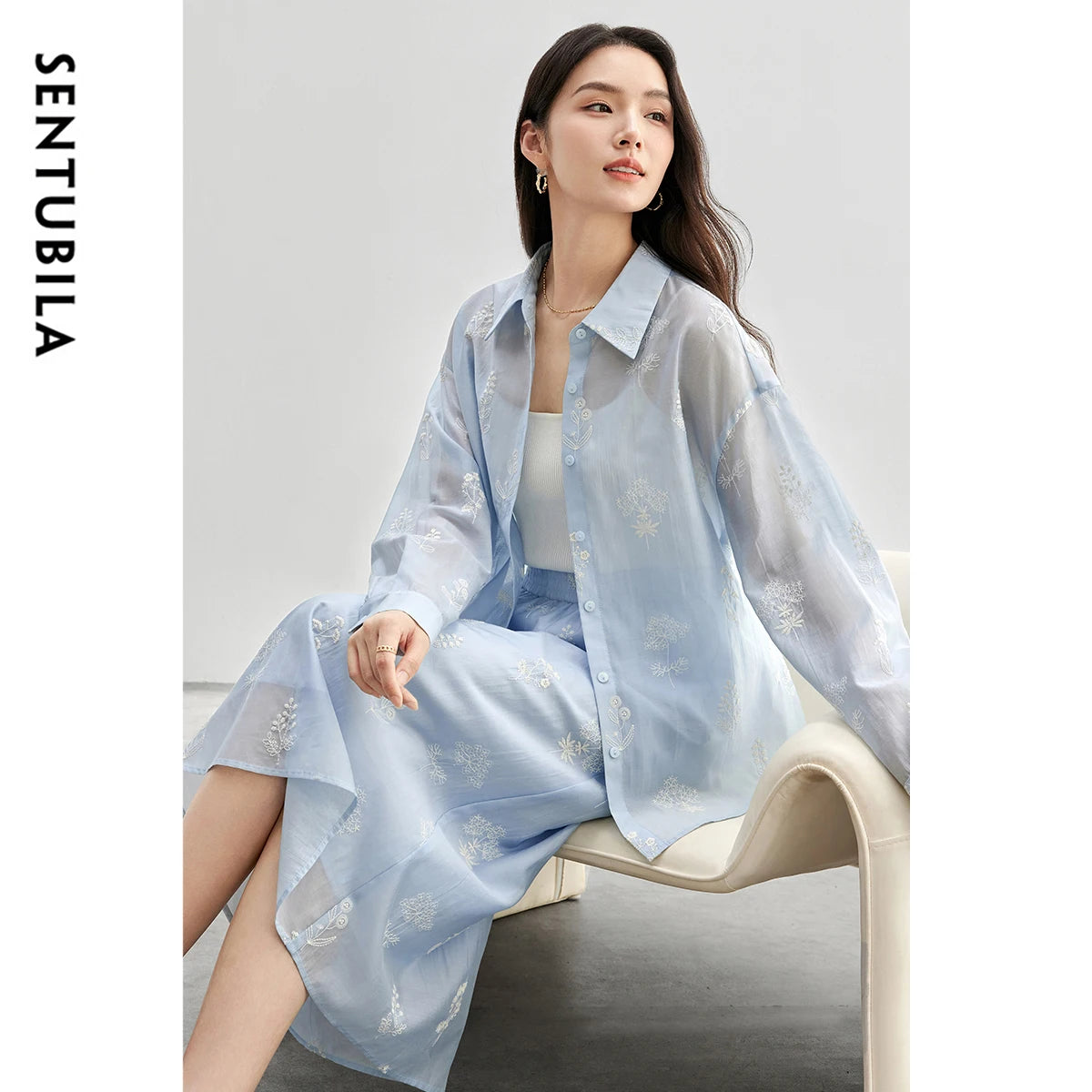 Woman wearing a light blue outfit with floral patterns, sitting on a chair against a plain background. SENTUBILA brand visible.