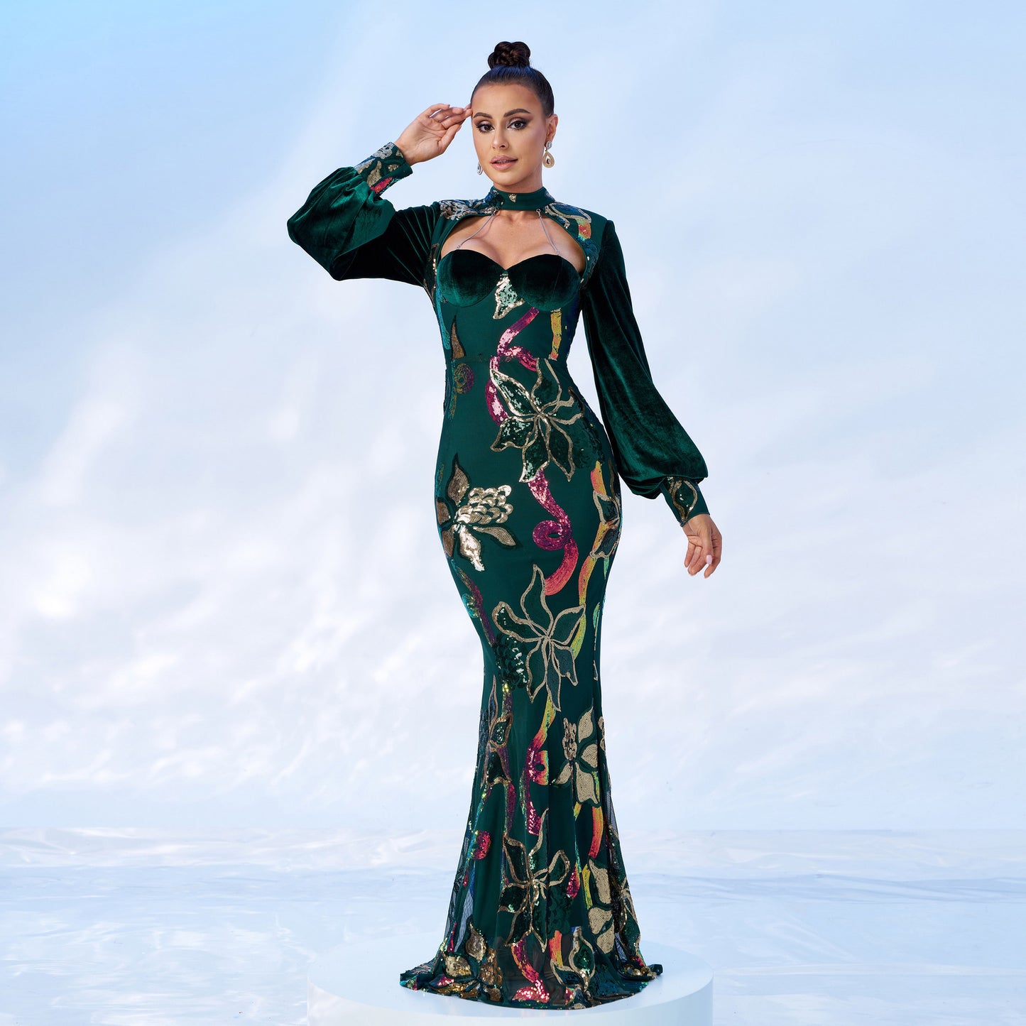 Woman wearing a green evening gown with floral patterns on a light blue background
