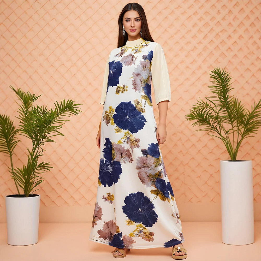 Woman wearing a floral dress standing between two potted plants against a patterned wall.